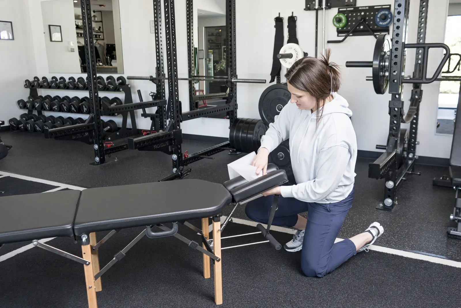 Dr. Abby Dante kneeling beside a treatment table on the training floor, rolling fresh paper over it