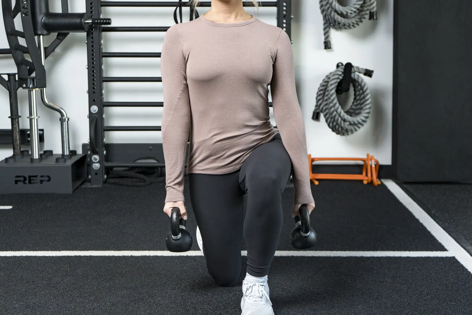 A person lowering into a lunge with a kettlebell in each hand on the clinic's training floor