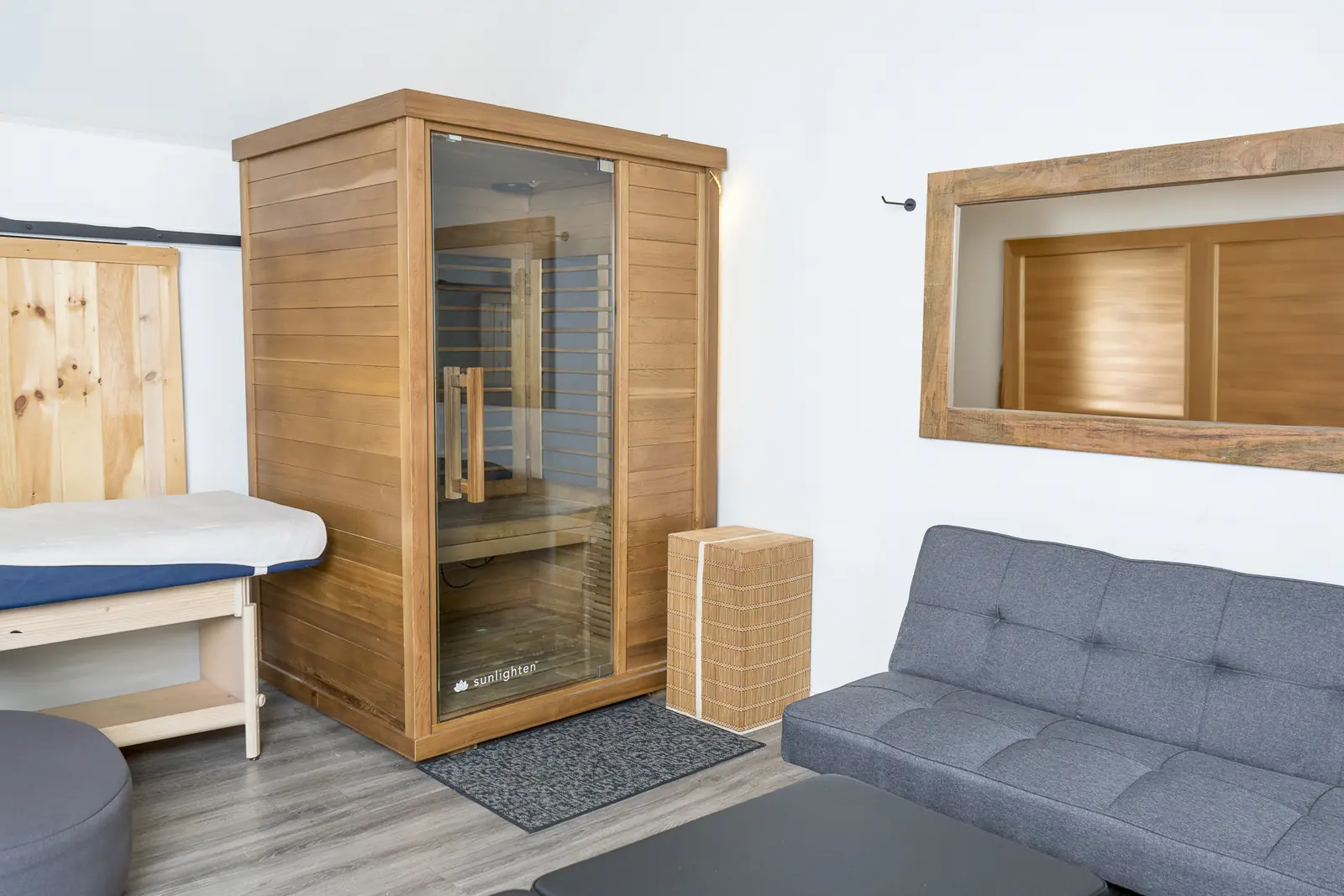A treatment room with a treatment table, a wood-panelled cabinet with a glass door and a grey couch