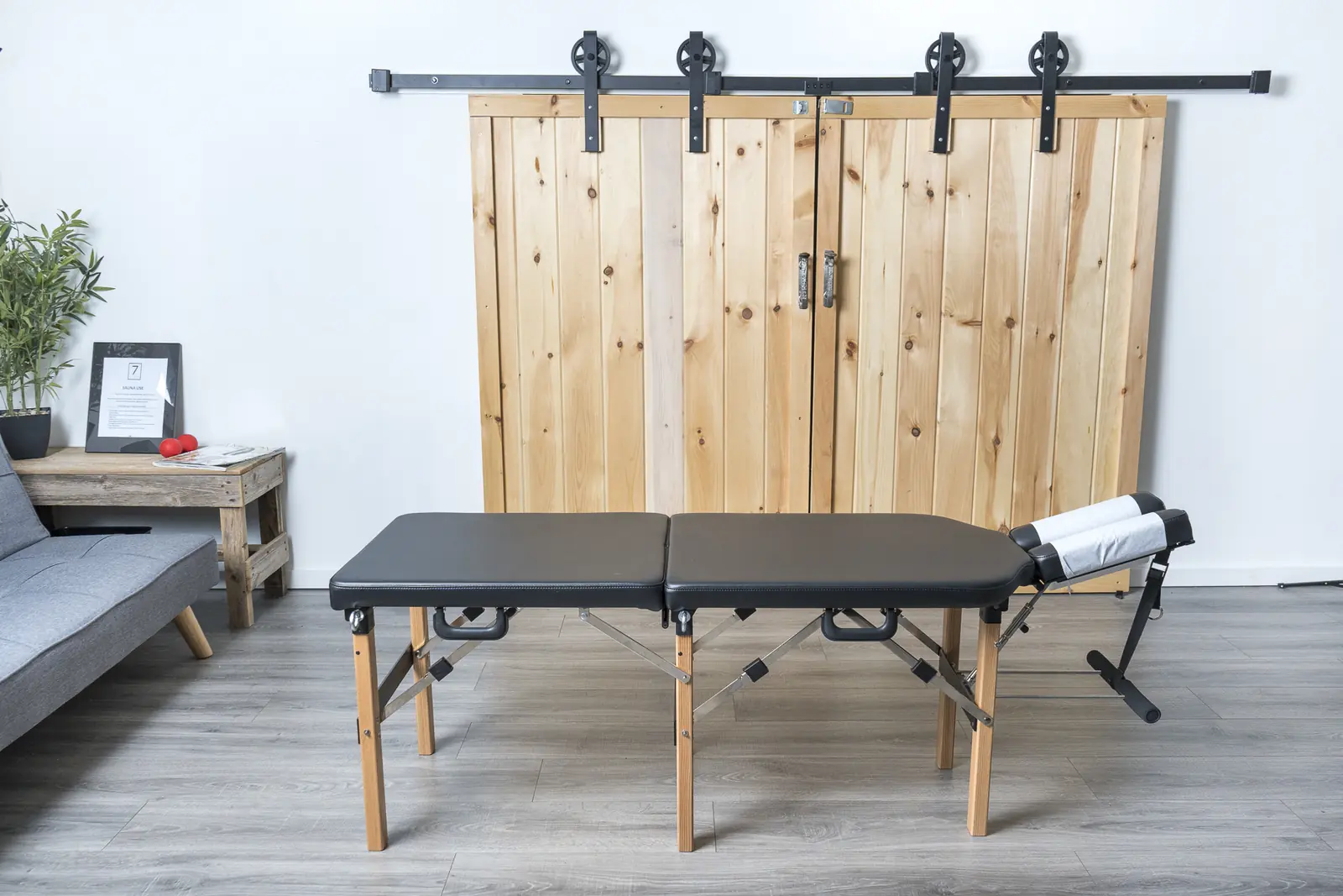 An empty treatment table in front of two sliding barn doors, beside a grey couch