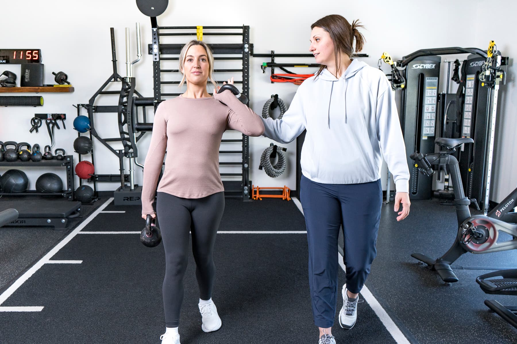 Dr. Abby Dante walking beside a patient who carries a kettlebell at her side across the clinic's training floor