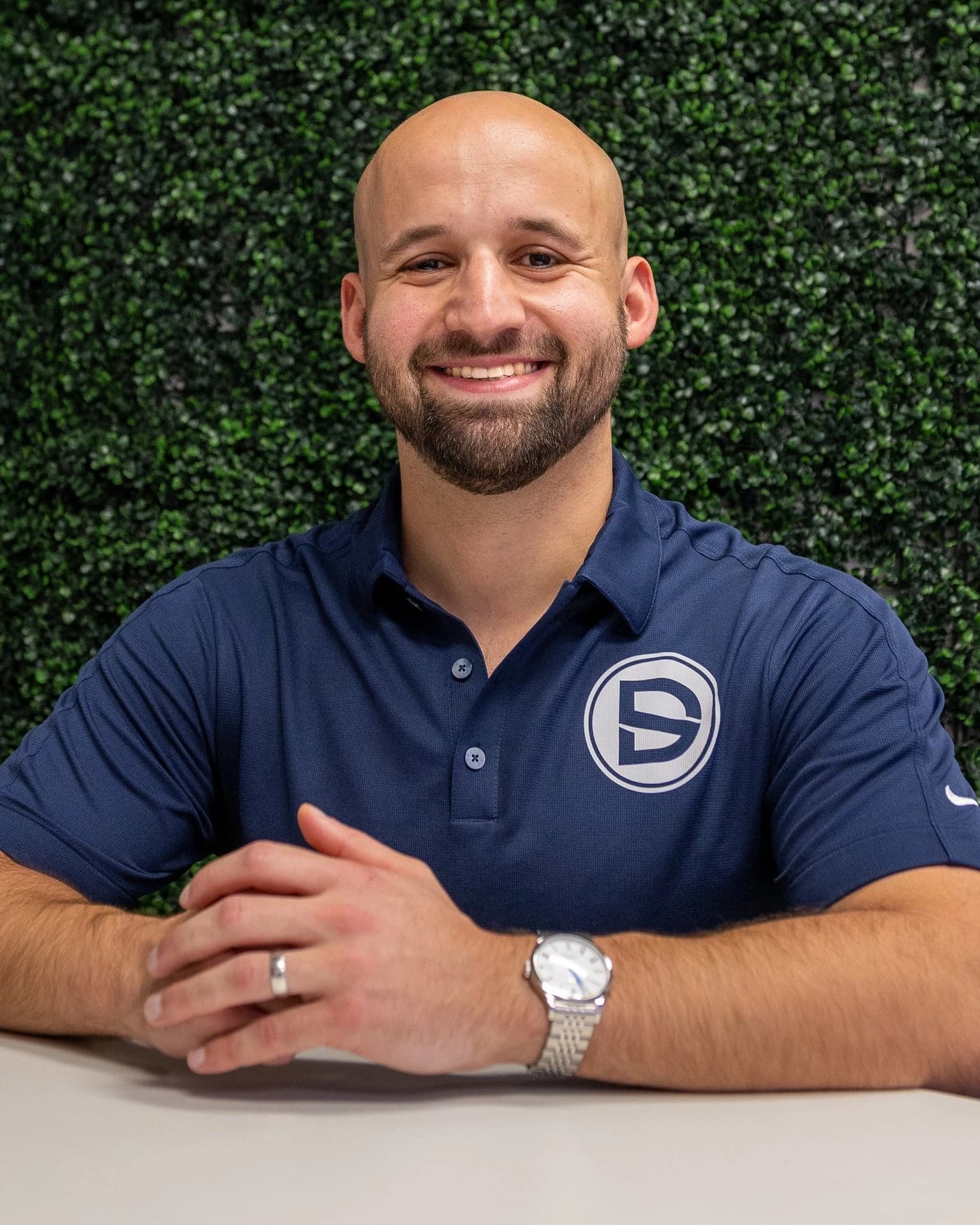 Dr. Dave Atlas in a navy Dante Sports polo, seated in front of a green boxwood wall