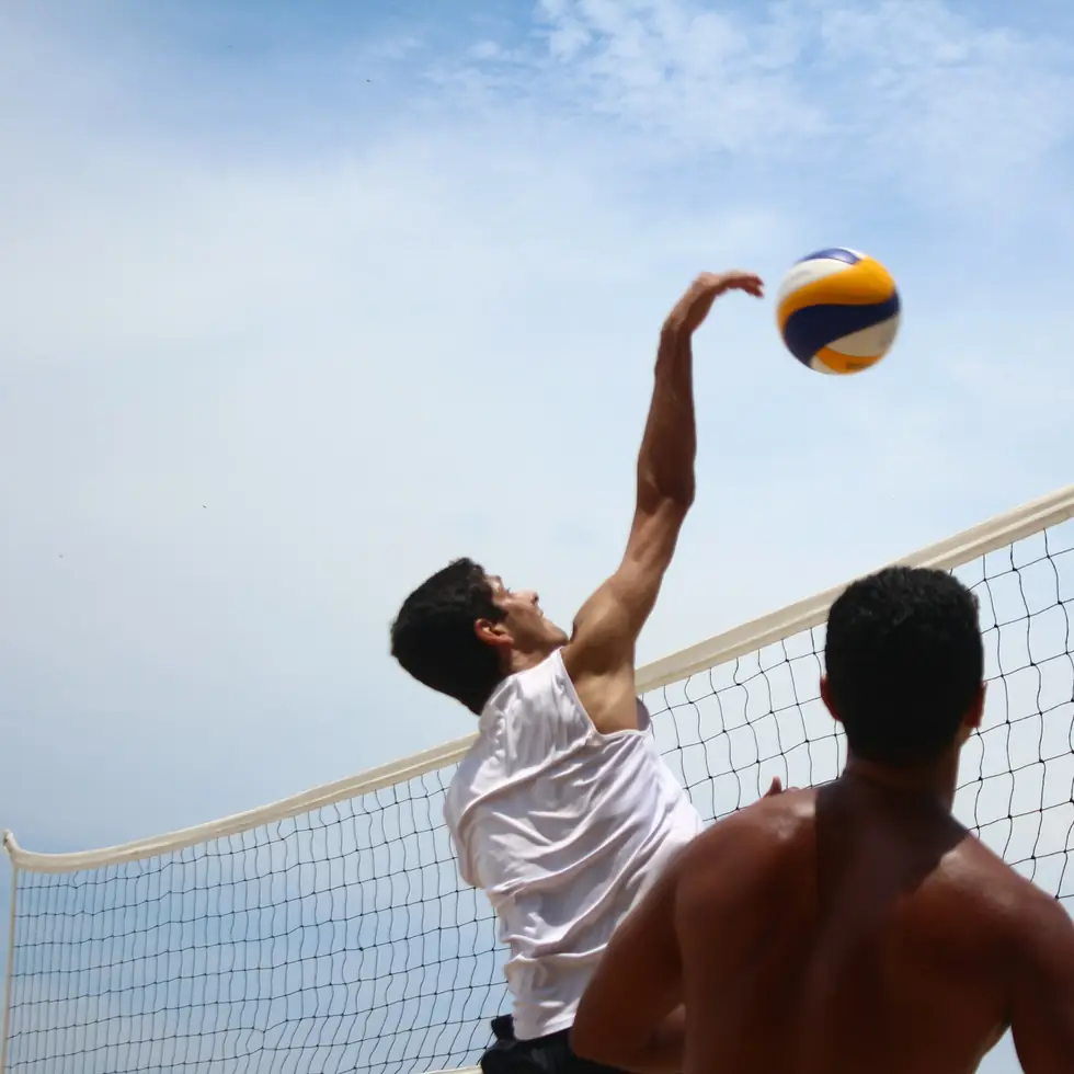 A volleyball player reaching overhead to spike the ball at the net