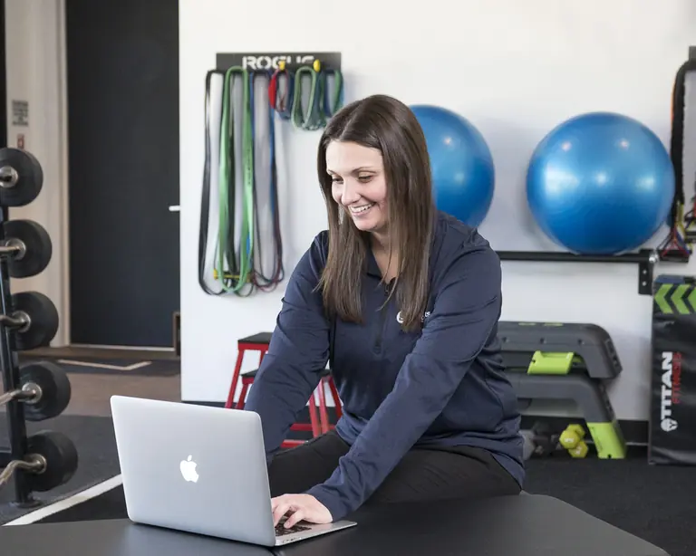 Dr. Abby Dante seated on a treatment table in the training area, typing on a laptop